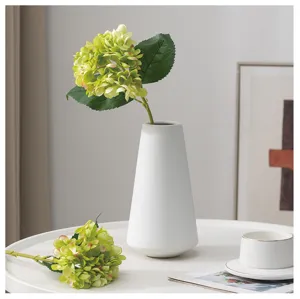 Primo piano dettagliato di un vaso in ceramica bianca con ortensie artificiali verdi.
