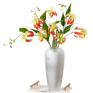 Arrangement de fleurs de lis gloriosa artificielles dans un vase blanc pour décoration.