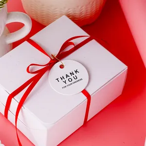 Scatola regalo bianca minimalista con nastro rosso e etichetta di ringraziamento.