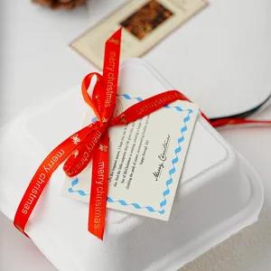 Detail shot of white paper gift box decorated with red merry christmas ribbon and greeting card.