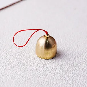 Kleine koperen bel met rood koord, ideaal voor DIY knutselen en feestelijke decoratie.