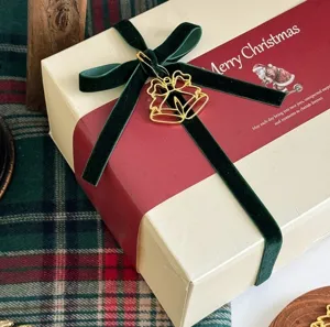 Christmas gift wrapping box with green velvet ribbon and gold bell pendant detail.