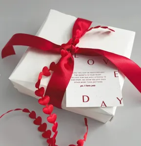 Primo piano di nastro di seta rossa e nastro a cuore su scatola regalo bianca per San Valentino.