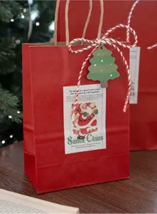 Dettaglio sacchetto regalo Natale in carta kraft rossa, confezione festiva con adesivo ed etichetta.