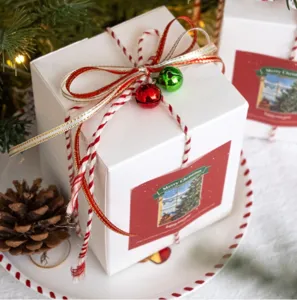 Weihnachtsgeschenkbox mit rot-weißem Kordelband, Schleifen und Glocken für Dekoration.
