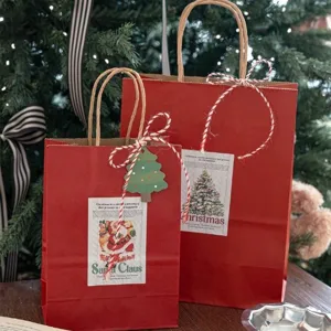 Sacchetti regalo di carta kraft rossa di Natale con manici ed etichette festive.