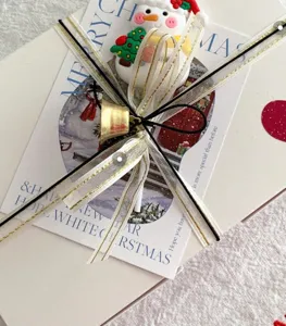 Kit d'emballage de cadeau de Noël avec cloche dorée, carte de bonhomme de neige et ruban.