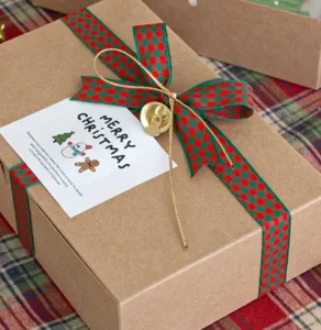 Christmas gift box packaging detail showing red green plaid ribbon bow and small bell.