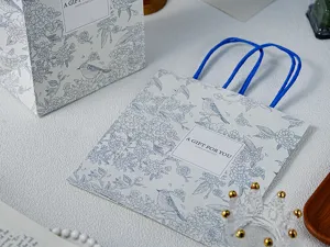 Close-up van decoratieve papieren cadeautas met bloemvogelontwerp en blauwe handvatten.