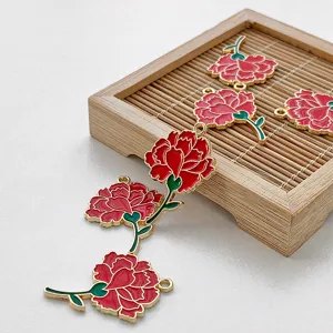 Detailed view of red enamel carnation flower metal charms with gold trim for DIY craft projects.