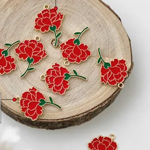 Close-up detail shot of red and green enamel carnation charms displayed on a natural wood slice prop.