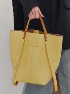 Yellow leather bucket bag detail showing contrast brown handle and spacious interior structure.