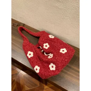 Detail shot of red fluffy tote bag featuring white floral embroidery on a wooden table.