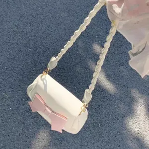 Detail view of the white cylindrical shoulder bag featuring a sweet pink bow and braided strap.