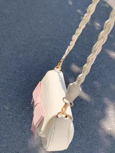 Detail view of a chic cream white women shoulder bag featuring a cute pink bow and braided strap.