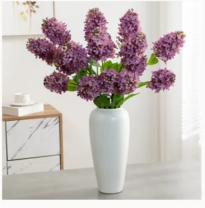 Kunstmatige paarse syringa bloemen in witte vaas detailweergave voor huisdecoratie.