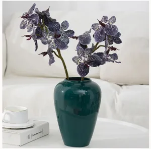 Artificial vanda orchid flower arrangement in dark green ceramic vase for home decor setup.