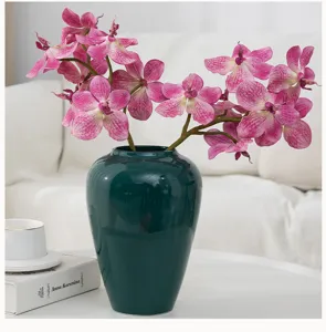 Artificial orchid flower arrangement in dark green ceramic vase for home decor wedding.