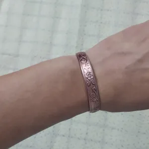 Primo piano dettagliato di un bracciale rigido in rame rosso vintage con motivo floreale.