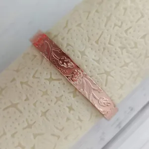 Primo piano dettagliato del bracciale in rame rosso con motivi floreali e di viti incisi.
