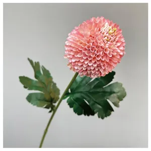Close-up detail of artificial pink pompon chrysanthemum flower head with green leaves stem.