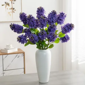 Kunstmatige paarse syringa bloemen in witte keramische vaas voor woonkamer decoratie.