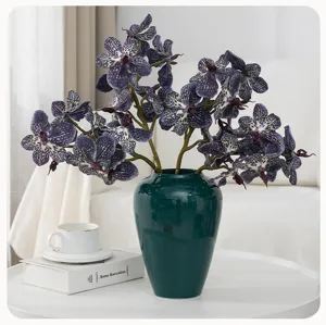 Artificial Phalaenopsis orchid arrangement in dark green ceramic vase home decor detail shot.