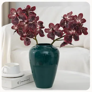 Detailed view of artificial orchid flower arrangement in dark green ceramic vase for home decor.