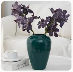 Artificial purple orchid flower arrangement in dark green ceramic vase for home decor