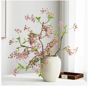 Vista dettagliata di un ramo di fiori artificiali con fiori rosa e foglie verdi in vaso bianco.