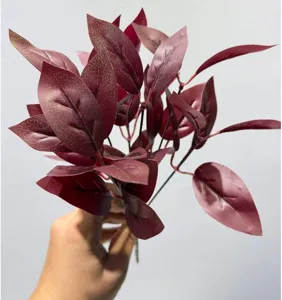 Primer plano detallado de una rama de hojas burdeos artificiales para decoración de interiores.