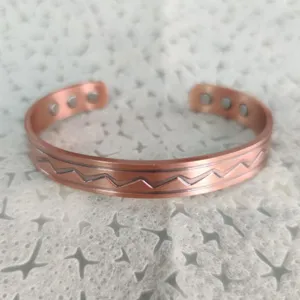 Primo piano di un elegante bracciale magnetico in rame con motivo a onde unico.