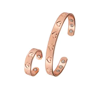 Primo piano dettaglio del bracciale rigido in rame magnetico e anello con motivo a cuore inciso.