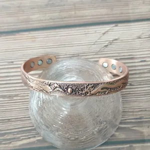 Vista dettagliata del bracciale magnetico in rame con motivo inciso di drago e fenice.