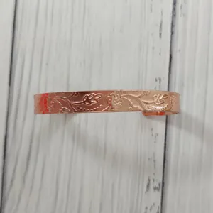 Primo piano dettagliato di un bracciale rigido in rame inciso con delicati motivi floreali.