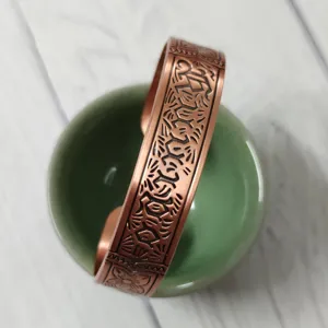 Detail view of wide vintage copper cuff bracelet with intricate carved floral patterns.