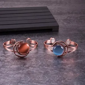 Detail shot of two open-cuff copper bracelets with magnetic ends and celestial cat's eye stones.