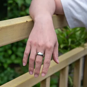 Detail view of a stylish wide faceted tungsten carbide ring worn on finger, minimalist style.