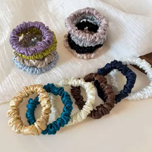 Close-up detail of multi-color satin silk hair scrunchies arranged neatly on white fabric.