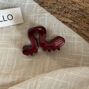 Gros plan détaillé de la pince à cheveux en acétate rouge foncé avec élégantes lettres.