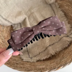 Detailed close-up of a brown fabric hair claw clip featuring a charming white floral print.