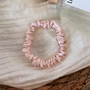 Silk scrunchie detail view, pink satin hair tie showing soft glossy fabric texture.