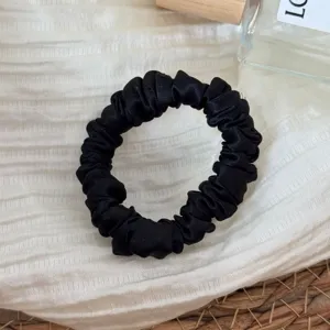 Detail view of a black silk hair scrunchie, satin material, elegant and gentle on hair.