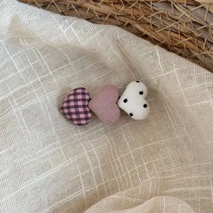 Primer plano detallado del lindo pasador de pelo de tela con corazón, cuadros y lunares.
