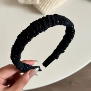 Dettaglio del cerchietto plissettato nero con trama in tessuto e pois colorati.