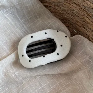 Vue détaillée d'une pince à cheveux en tissu blanc à pois noirs sur fond textile beige.