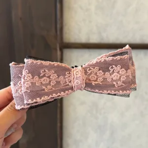 Détail de pince à cheveux nœud en dentelle filet rose brodé et tulle noir superposé.
