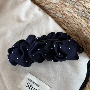 Gedetailleerde close-up van een elegante donkerblauwe haarspeld met witte polkadots.