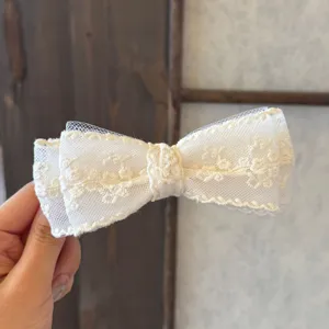 Gros plan sur le nœud papillon en résille de dentelle ivoire, broderie florale fine.