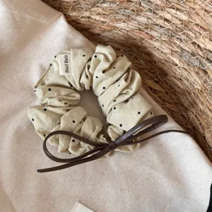 Gedetailleerd overzicht van beige haarscrunchie met stippen en een bruine leren strik.